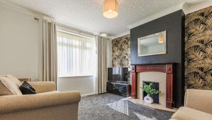 A living room with two beige sofas, a fireplace, and a large window with curtains. - Comfy house in Thornaby, Stockton On Tees (Thornaby on Tees)