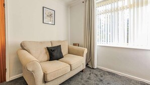 A beige sofa with a black pillow in a room with a window, a framed picture on the wall, and a door. - Comfy house in Thornaby, Stockton On Tees (Thornaby on Tees)