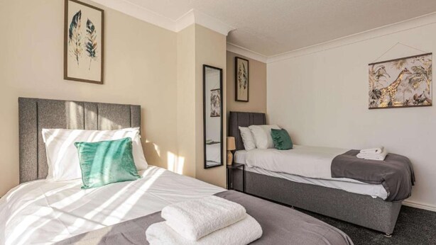 A hotel room with two beds, each with a grey headboard and white bedding. There are framed artworks on the walls and a large painting above the beds. - Comfy house in Thornaby, Stockton On Tees (Thornaby on Tees)