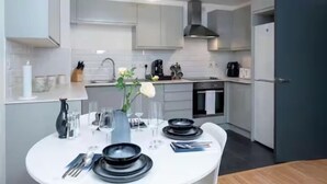 Une cuisine moderne avec des meubles blancs, une table à manger dressée avec des assiettes noires et un vase rempli de fleurs.