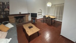 Una sala de estar con chimenea, televisor, mesa de comedor con sillas y estantería.