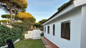 Un edificio blanco con base de ladrillo, un pequeño jardín con césped y seto, y una parrilla negra.