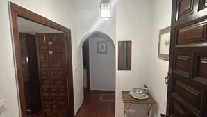 Un pasillo con una puerta de madera a la derecha, una mesita con platos y una lámpara colgante.