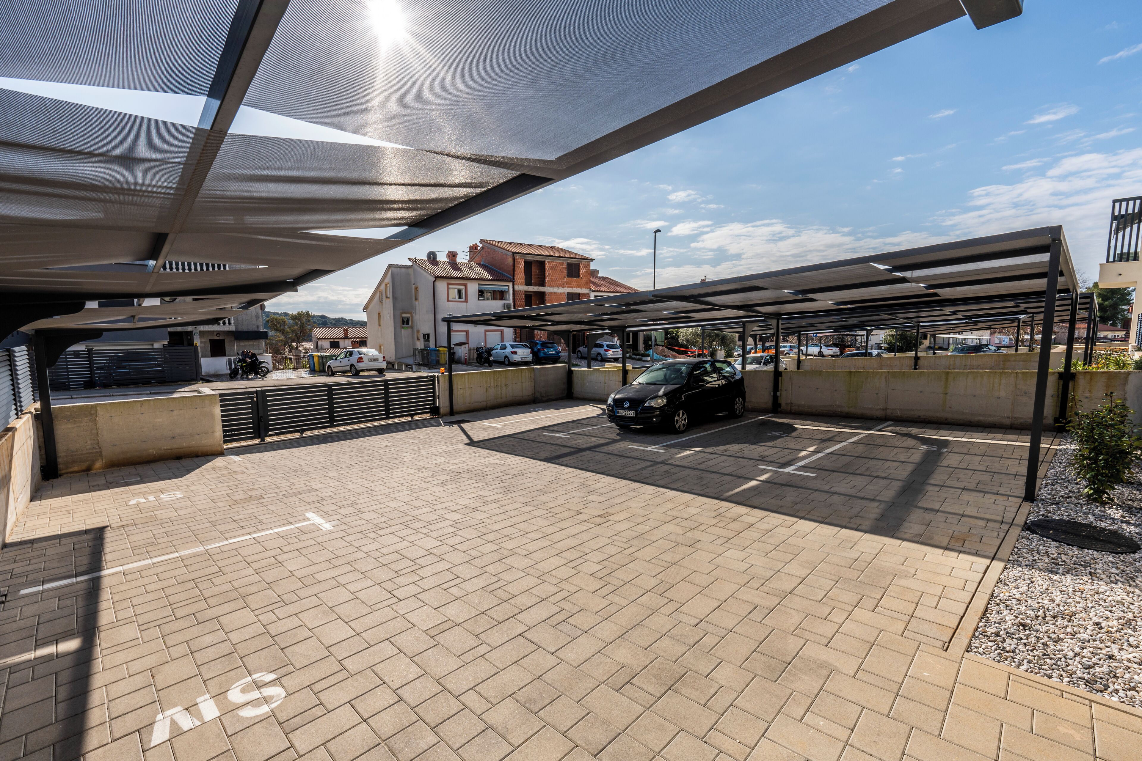 A parking area with covered carports, a paved walkway, and a building in the background.