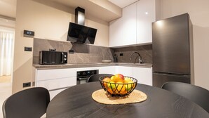 A modern kitchen with a dark wooden table, a bowl of fruit, a microwave, a stove, and a refrigerator. - Apartment Tissa (Pula)