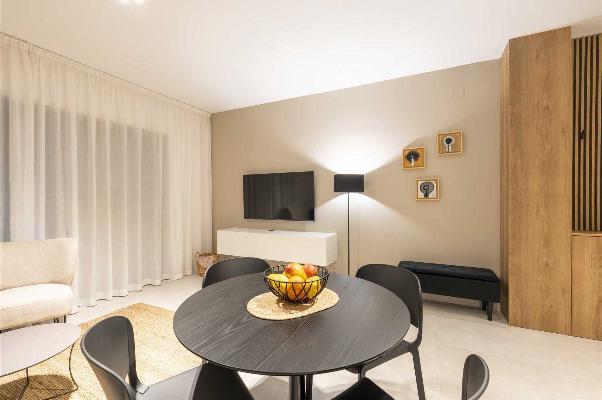 Un salon moderne avec une table à manger ronde, des chaises noires, un canapé, un téléviseur et un mur d’accent en bois.