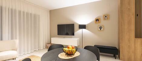 Un salon moderne avec une table à manger ronde, des chaises noires, un canapé, un téléviseur et un mur d’accent en bois.
