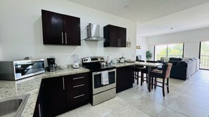 A modern kitchen with dark cabinetry, a built-in oven, and a dining area with a table and chairs. - Jaco Bay 5701 (Jaco Beach)