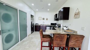 A modern kitchen with a dining area, featuring a kitchen island, bar stools, and a sliding glass door leading to a balcony. - Jaco Bay 5701 (Jaco Beach)