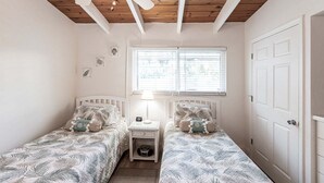 A bedroom with two single beds, a bedside table with a lamp, a window with blinds, and a door. - 19 Premium Plus - Coastal Comfort (Sarasota)