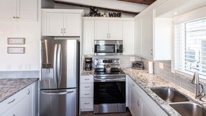A modern kitchen with white cabinets, stainless steel appliances, a granite countertop, and a window with blinds. - 19 Premium Plus - Coastal Comfort (Sarasota)