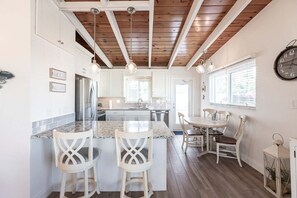 A kitchen with a central island, bar stools, a dining table with chairs, and a clock on the wall.