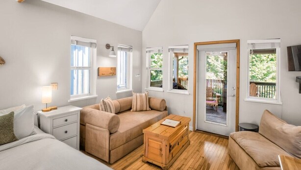 Amplia sala de estar con un sofá grande, una mesa de centro de madera y una mesa de comedor. Varias ventanas ofrecen luz natural y vistas al exterior.