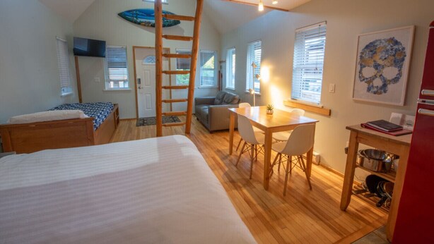 Una habitación con dos camas, una mesa de comedor con sillas, una escalera y una kitchenette.