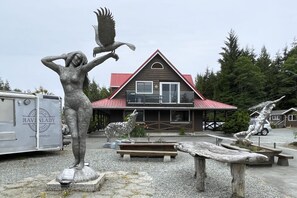 A rustic lodge with a red roof, a wooden deck, and a statue of a wolf. - Raven Lady Suite #202, Downtown Ucluelet (Ucluelet)