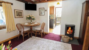 Une pièce chaleureuse avec une table ronde en bois, deux chaises, une cheminée et un téléviseur fixé au mur.
