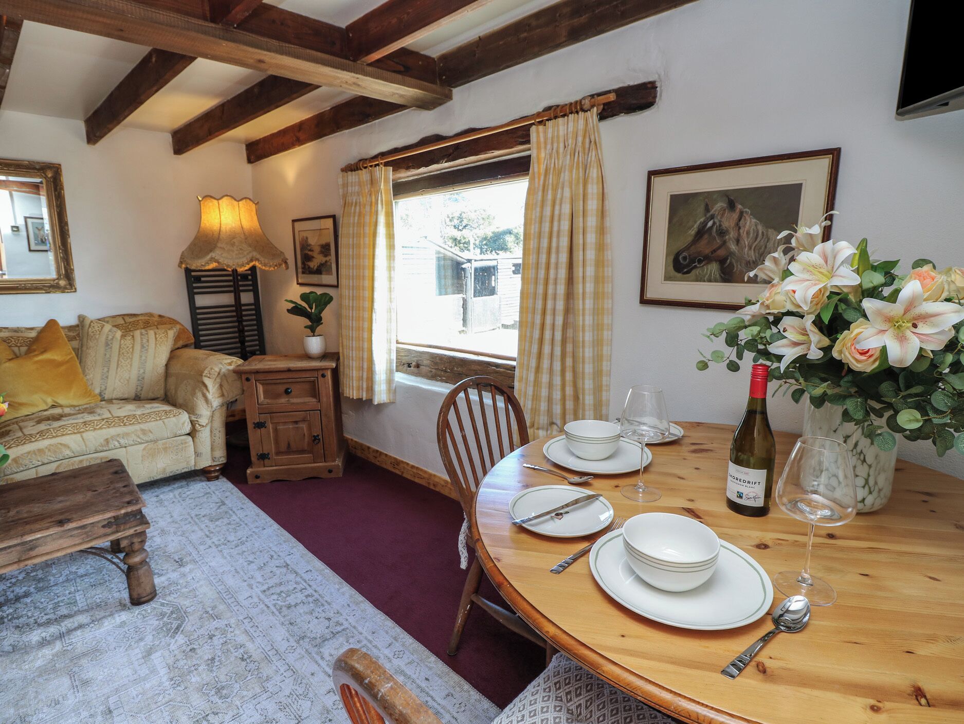 A dining area with a wooden table set for four, a sofa, a lamp, and a window with curtains.