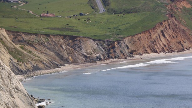 Un paysage côtier avec des falaises, une plage et une route sinueuse.