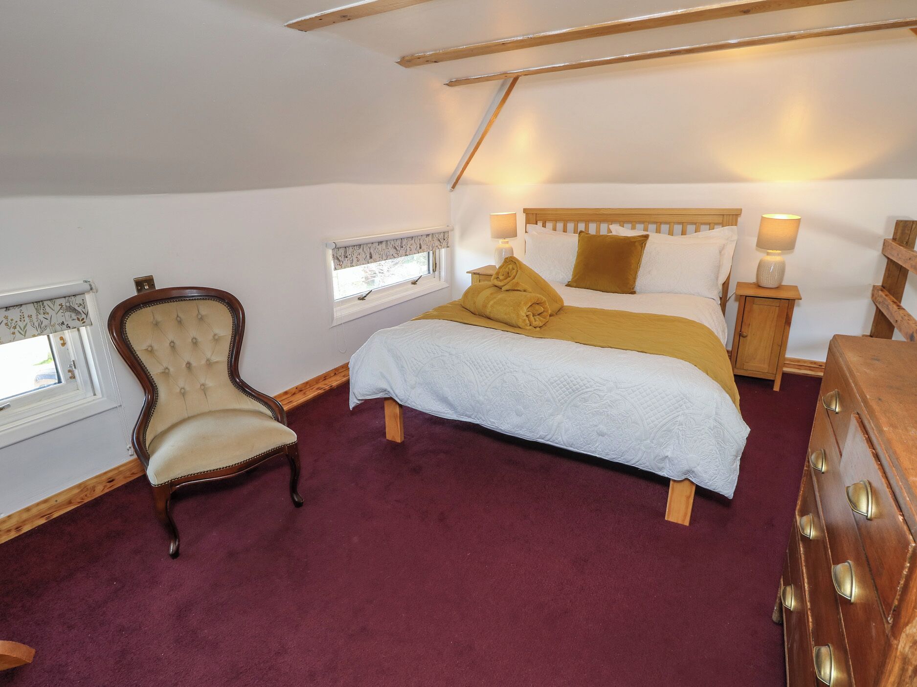 A bedroom with a bed, a wooden nightstand, a chair, and a window with a curtain.