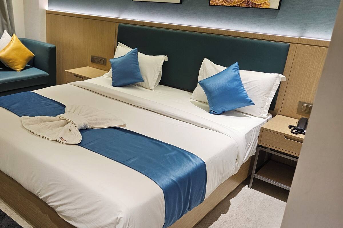 Hotellihuone, jossa on suuri sänky, kaksi yöpöytää, yölamppu, sininen sohva ja ikkuna, jossa on verhot.