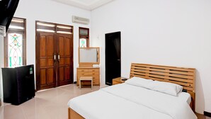 Ein Schlafzimmer mit einem Bett, einer Holzkommode, einem Spiegel, einem Fernseher und einer Tür mit Glasmalerei.