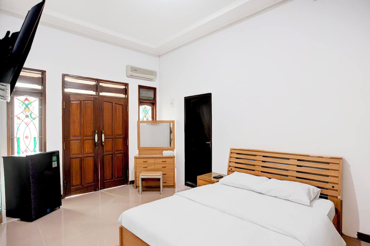 A bedroom with a bed, a wooden dresser, a mirror, a television, and a door with stained glass windows.