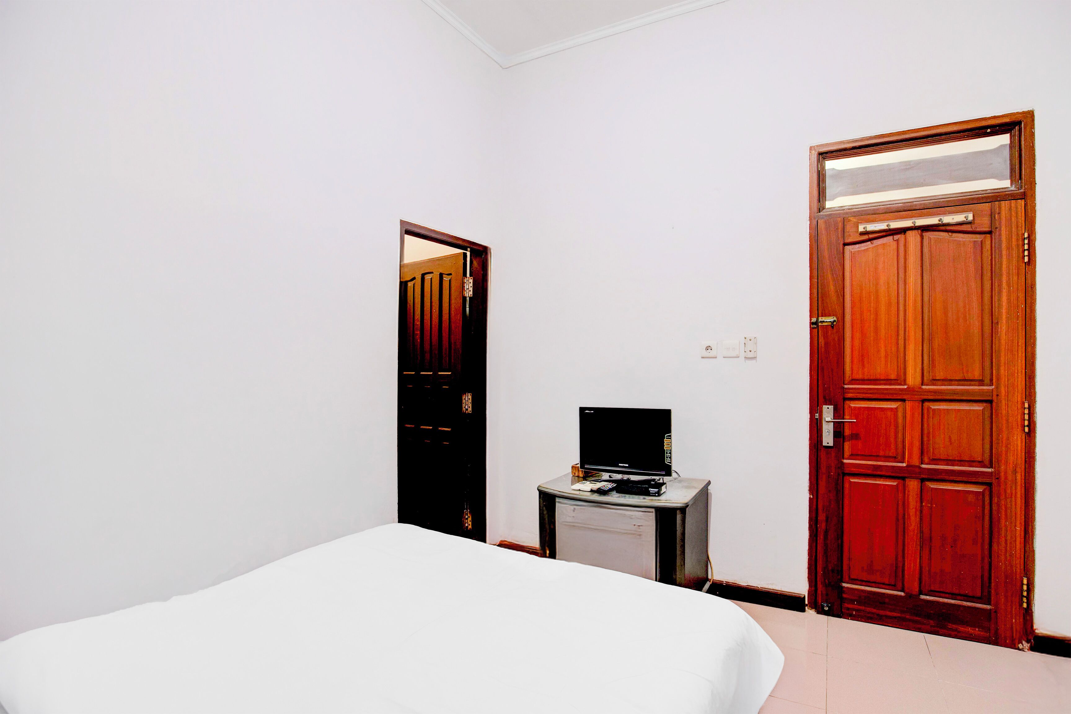 A hotel room with a bed, a small table with a television, and two wooden doors.