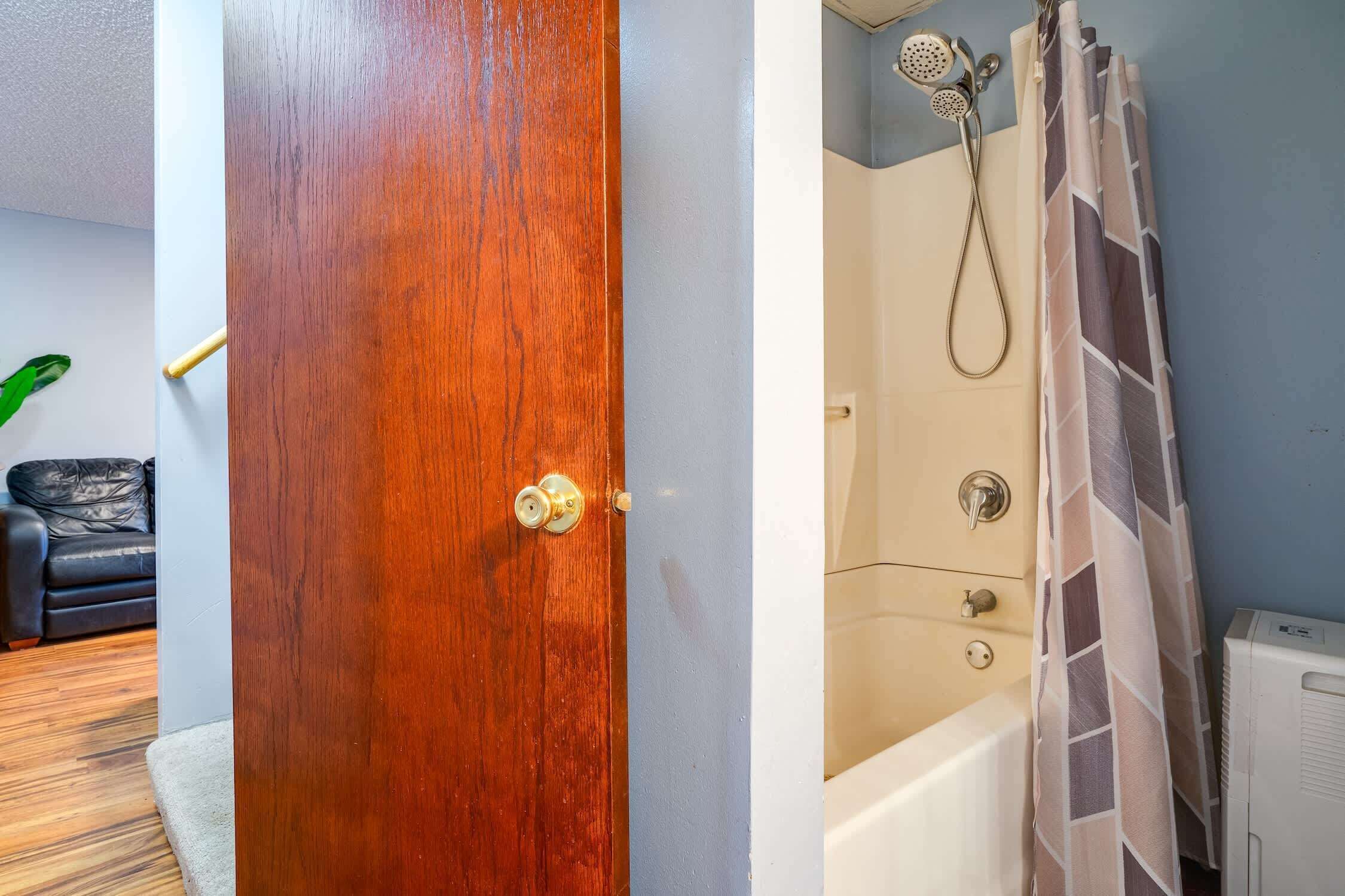 Puerta de madera que da a un baño con ducha, un perchero y un radiador.
