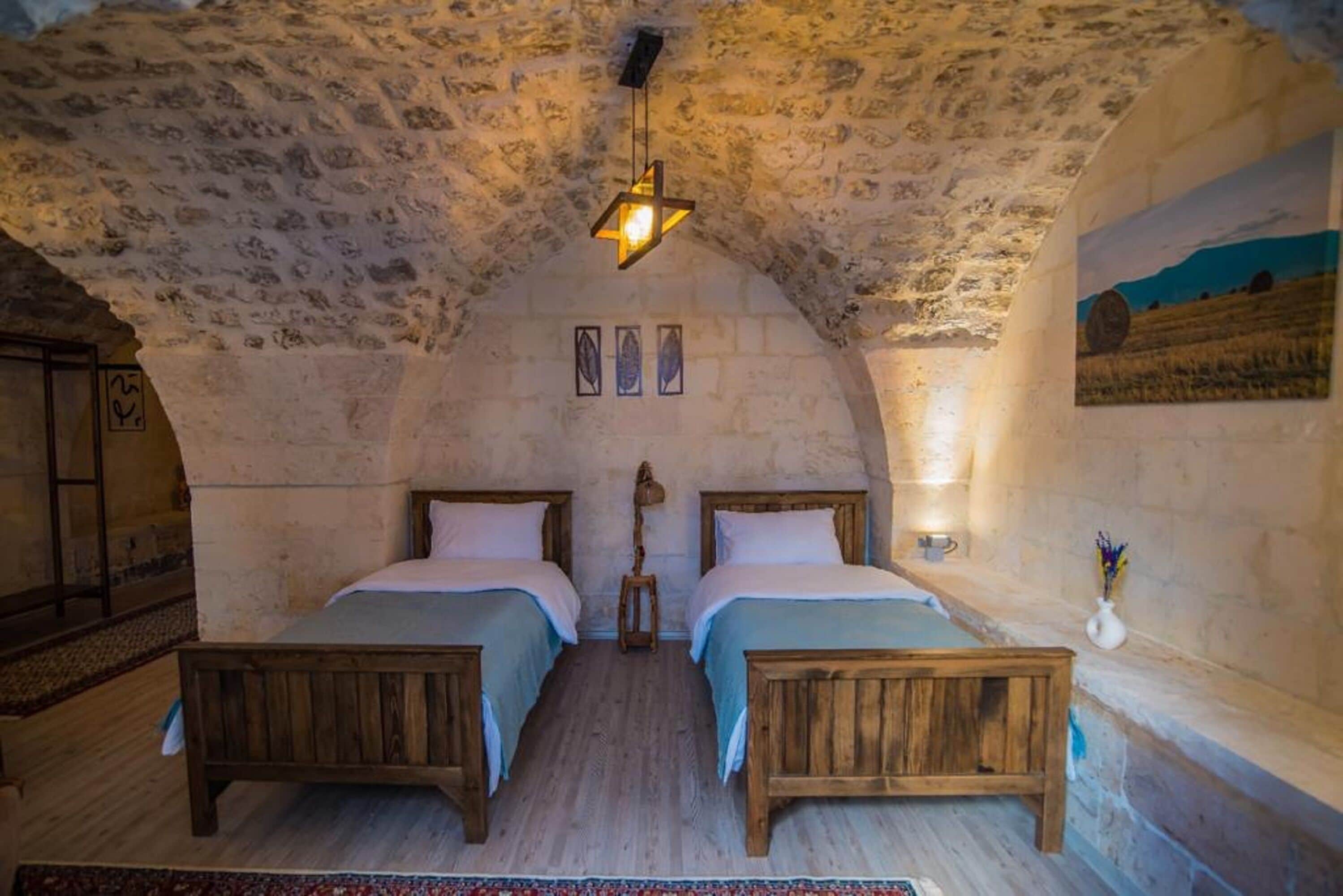 Una habitación rústica con dos camas de madera, techo de piedra y un cuadro en la pared.