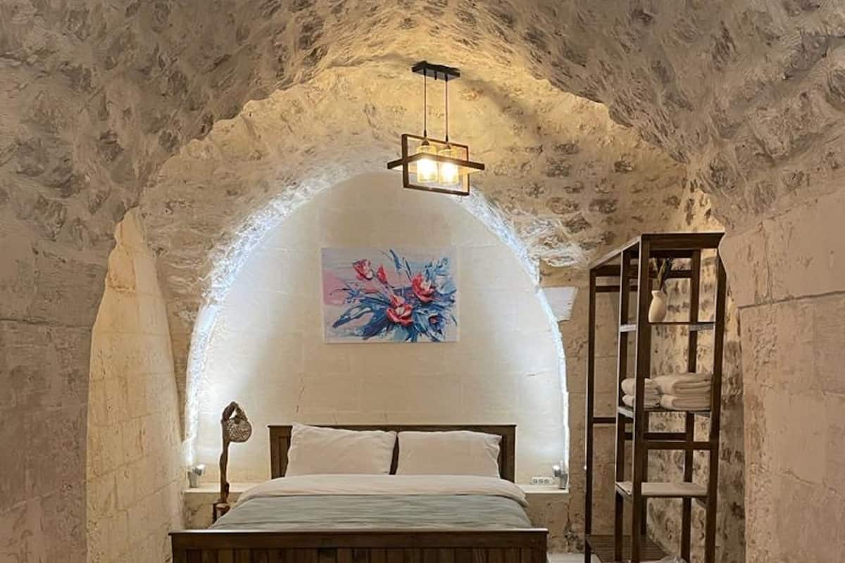Une chambre avec un plafond en pierre en forme d’arc, un lit en bois, une chaise blanche, un tapis à motifs et un tableau accroché au mur.