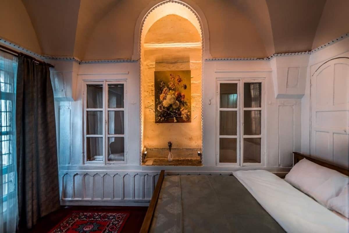 Une chambre avec un grand lit, une fenêtre avec des rideaux, un radiateur et un tableau au-dessus du lit.