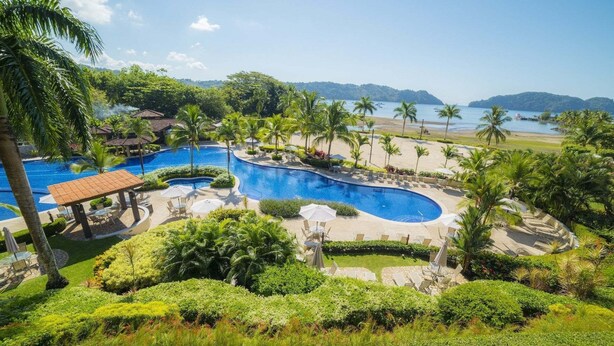 Ein Resort mit großem zentralen Pool, Palmen und Blick auf den Strand.
