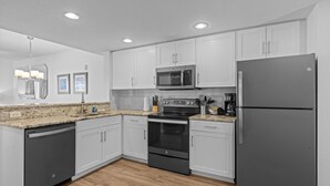 Una cocina moderna con armarios blancos, un refrigerador de acero inoxidable, un microondas, un horno y un lavavajillas.