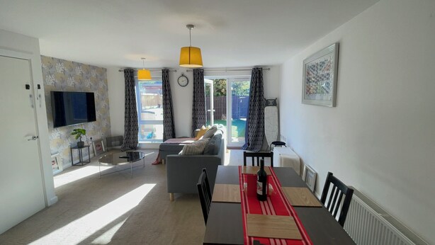 A modern living room with a sofa, a dining table, and a TV mounted on the wall.