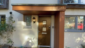 A modern building with a wooden door, a small window, and a wall-mounted light fixture.