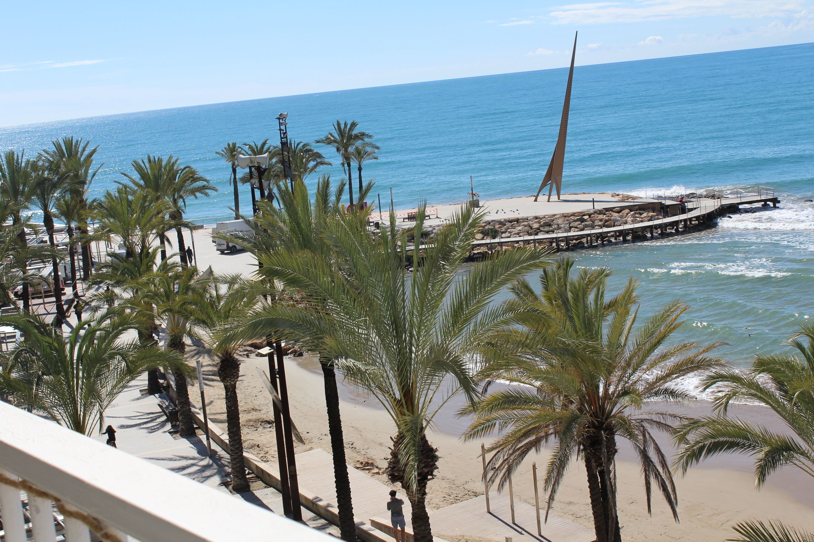 Una playa con palmeras, un muelle y un monumento alto.