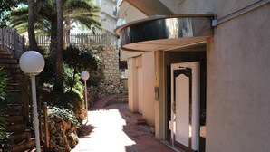 A pathway leading to a building entrance with a stone wall, palm trees, and a wooden fence. - Incredible first line Levante beach Salou (Salou)