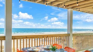 A wooden deck with a table set for dining, overlooking a beach with the ocean and a ship in the distance. - Dog-Friendly Beachfront Home with Pool (Gulf Shores)