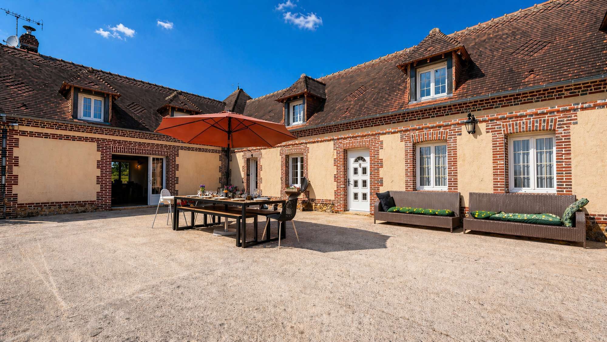 Une cour avec une table et des chaises, un canapé et un parasol.