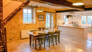 A rustic interior with a dining area, kitchen, and a staircase with exposed beams.
