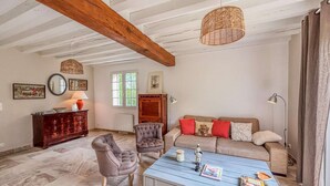 A living room with a blue coffee table, two armchairs, a sofa with red and beige cushions, a wooden cabinet, and a hanging wicker light fixture.