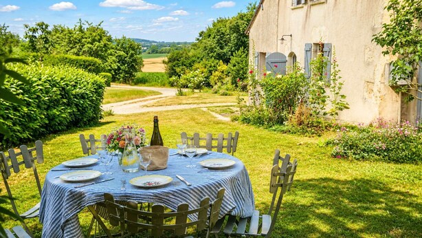 A round table set outdoors with a bottle, glasses, and plates, surrounded by chairs.
