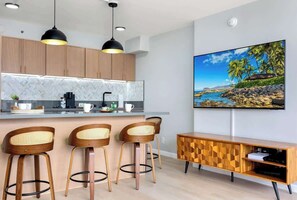 Une cuisine moderne avec des meubles en bois, un dosseret en motif chevrons et un coin bar avec des tabourets.