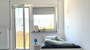 A modern bedroom with a bed, a window with blinds, a small bedside table, and a view of the outside. - Apartment with balcony, Stein near Nuremberg (Stein)