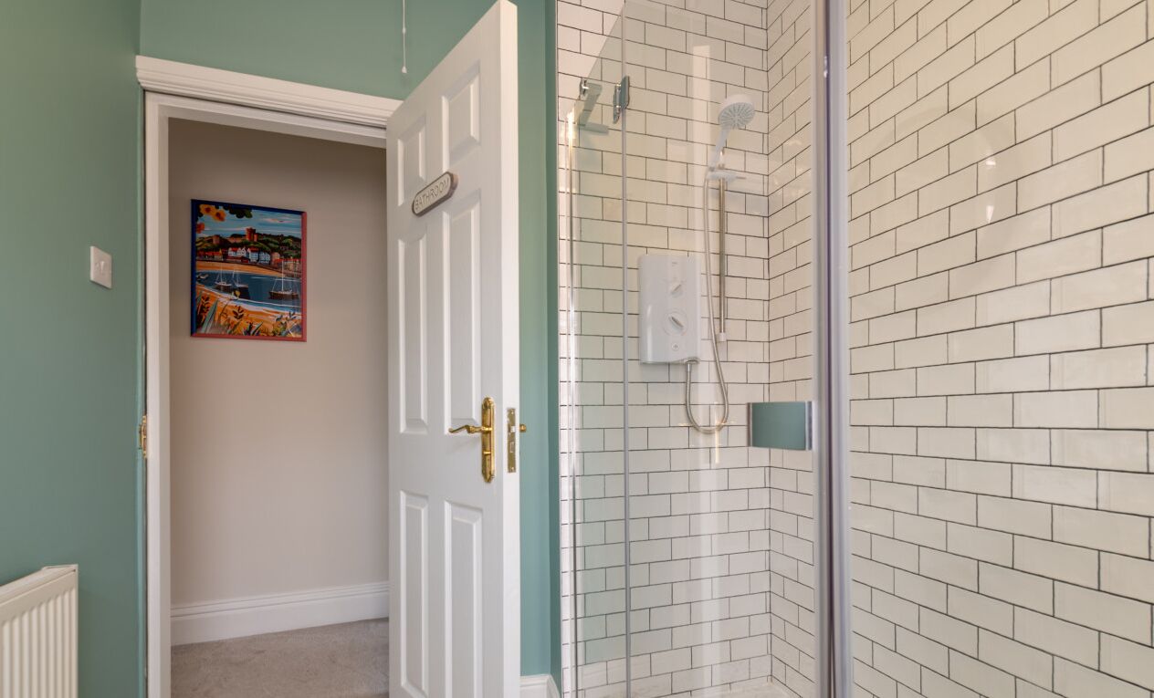 Une salle de bain avec une douche, une porte dotée d’une poignée en laiton et un mur recouvert de carreaux.