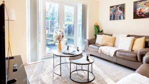 A living room with a sofa, two coffee tables, and a large window with a view of the outdoors. - Spacious 4-bed, Free Parking, Short or Long Stays (Manchester)