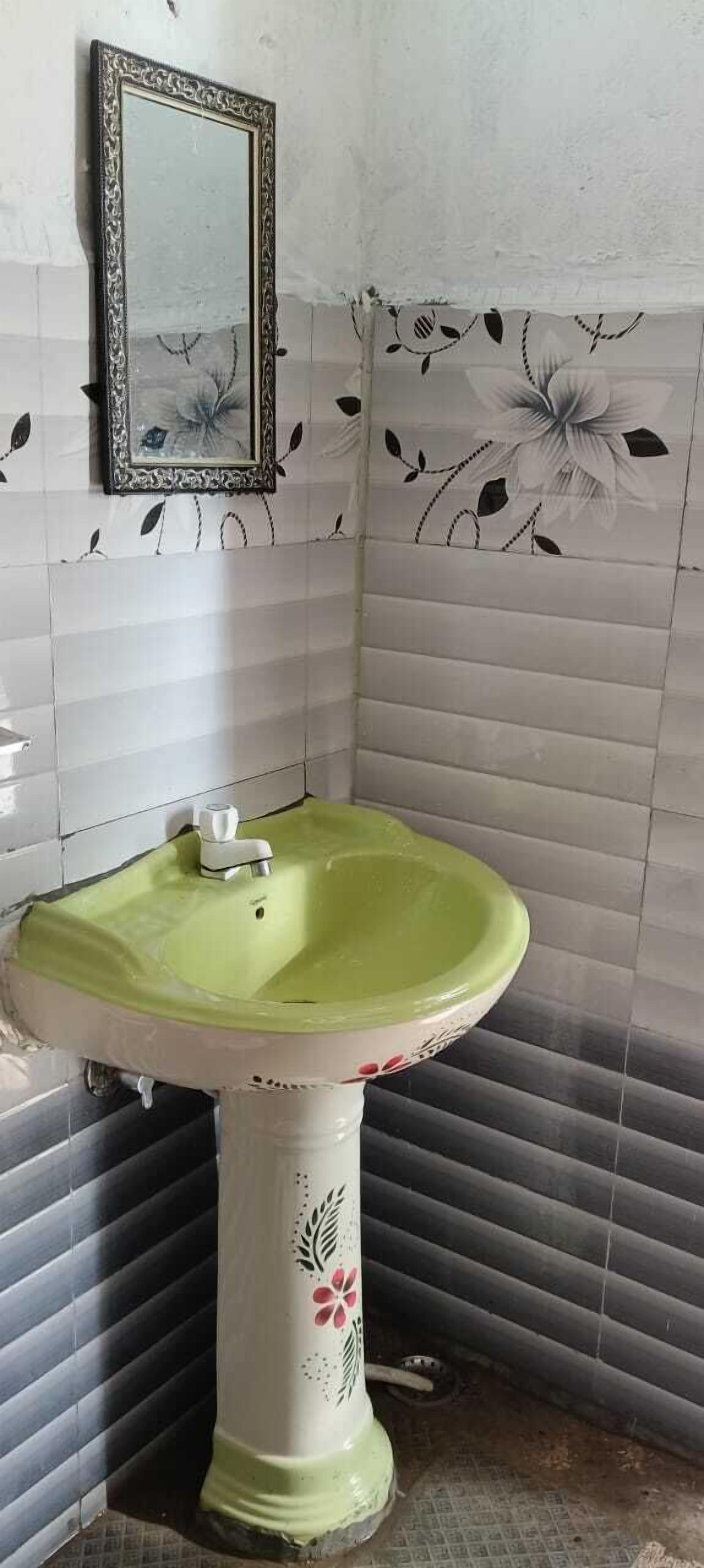 A bathroom with a green sink, a mirror, and floral wall tiles.
