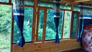 Una habitación con marco de ventana de madera, cortinas, una cama con colcha estampada y vistas al exterior con vegetación.