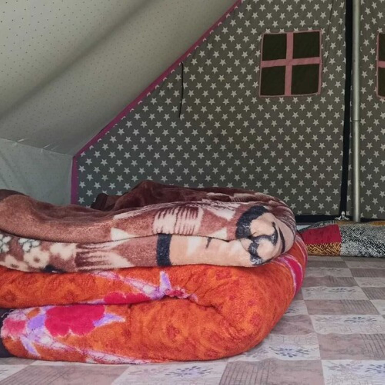 Ein Zelt mit Sternenmuster und kleinem Fenster, eine rote und braune Decke sowie ein karierter Boden.