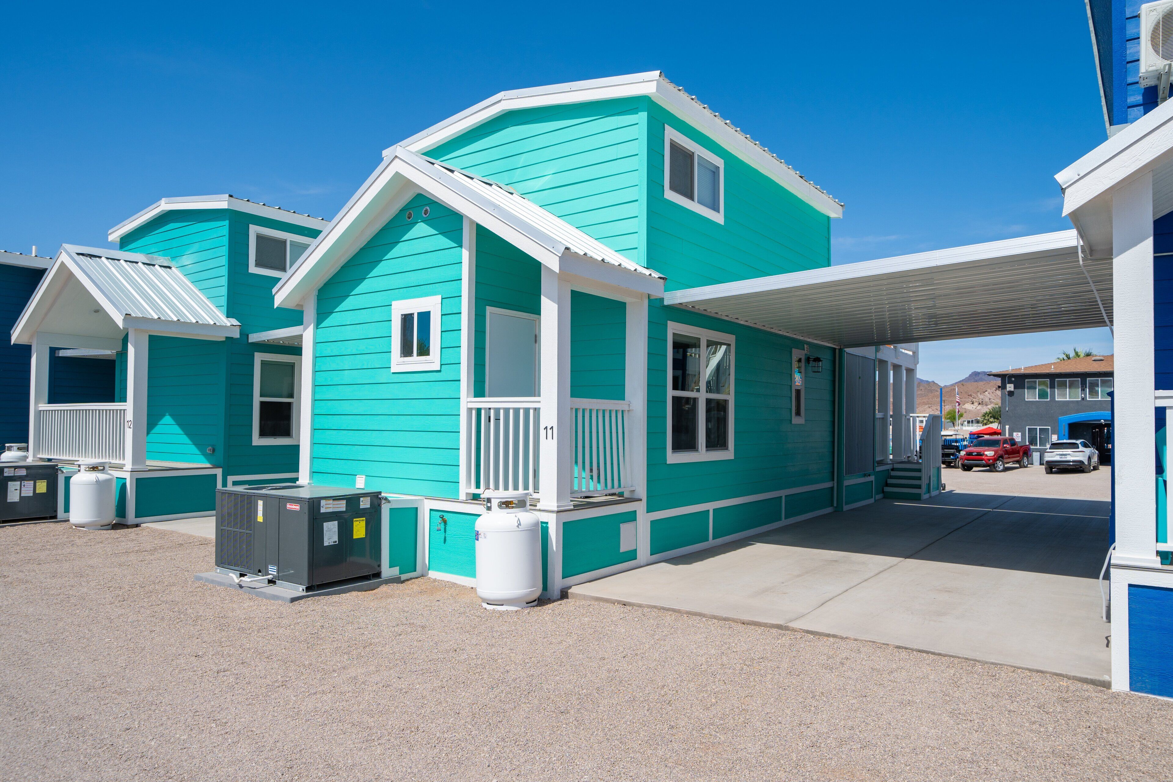 A row of turquoise buildings with white trim, featuring a covered parking area and visible air conditioning units.